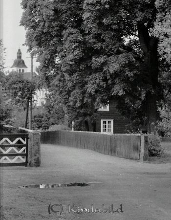 Värgården Kisa
gepe
Röd mangårdsbyggnad bakom ett stort vårdträd. Ett rött spjälstaket omsluter trädgården. 
Nyckelord: Värgården Kisa