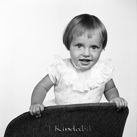 Annika och Carina Wiktorsson Kisa
gepe
En liten flicka i 3-4 årsådern klädd i klänning med volang, står på lnä bakvänt i en stol.
Nyckelord: Wiktorsson Kisa
